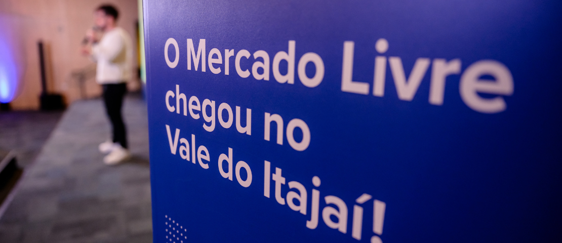 Gabriel Bollico no palco durante a inauguração do Polo de Moda do Mercado Livre no Vale do Itajaí, com destaque para material impresso que anuncia a chegada do projeto à região.
